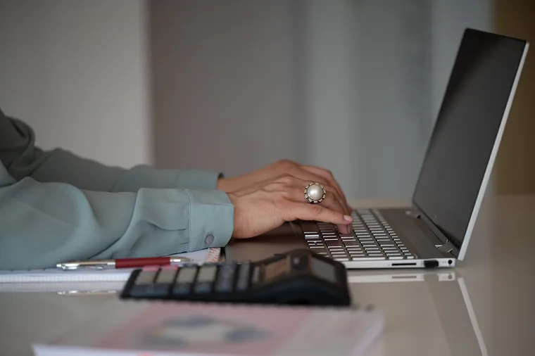 Hände am Laptop mit Taschenrechner und Buchhaltungsunterlagen